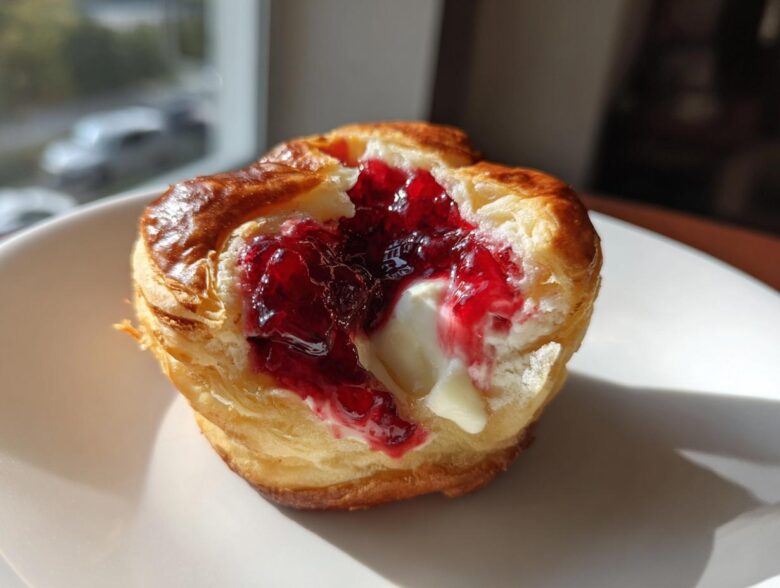 A close-up of a baked brie bite showing melted brie cheese and bright red jam inside flaky pastry.