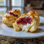 Close-up of warm brie bites showing melted brie cheese and bright red jam topping inside flaky pastry.