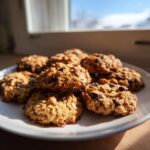 A stack of golden brown, oatmeal chocolate chip breakfast cookie treats piled on a white plate near a sunny window.