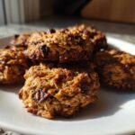 A small stack of golden brown, textured breakfast cookie treats featuring visible oats and dark fruit pieces on a white plate.