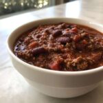 Close-up of a white bowl filled with rich, hearty chili containing ground meat and kidney beans.