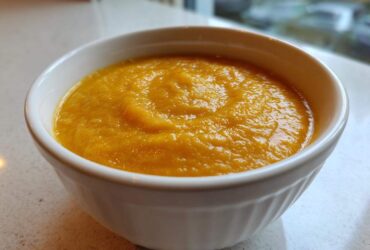A close-up of a white bowl filled with thick, vibrant orange pumpkin soup, ready to eat.