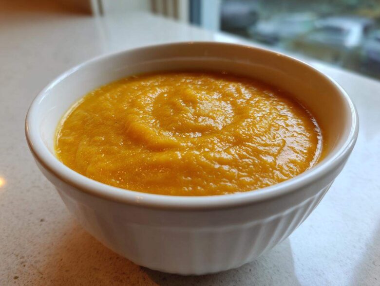 A close-up of a white bowl filled with thick, vibrant orange pumpkin soup, ready to eat.