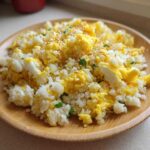A close-up of amazing cauliflower fried rice mixed with scrambled egg, topped with sesame seeds, served on a wooden plate.