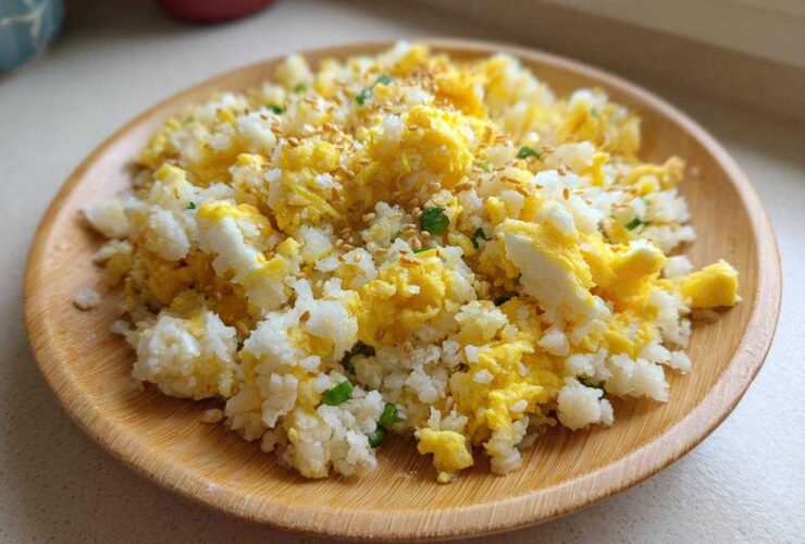 A close-up of amazing cauliflower fried rice mixed with scrambled egg, topped with sesame seeds, served on a wooden plate.