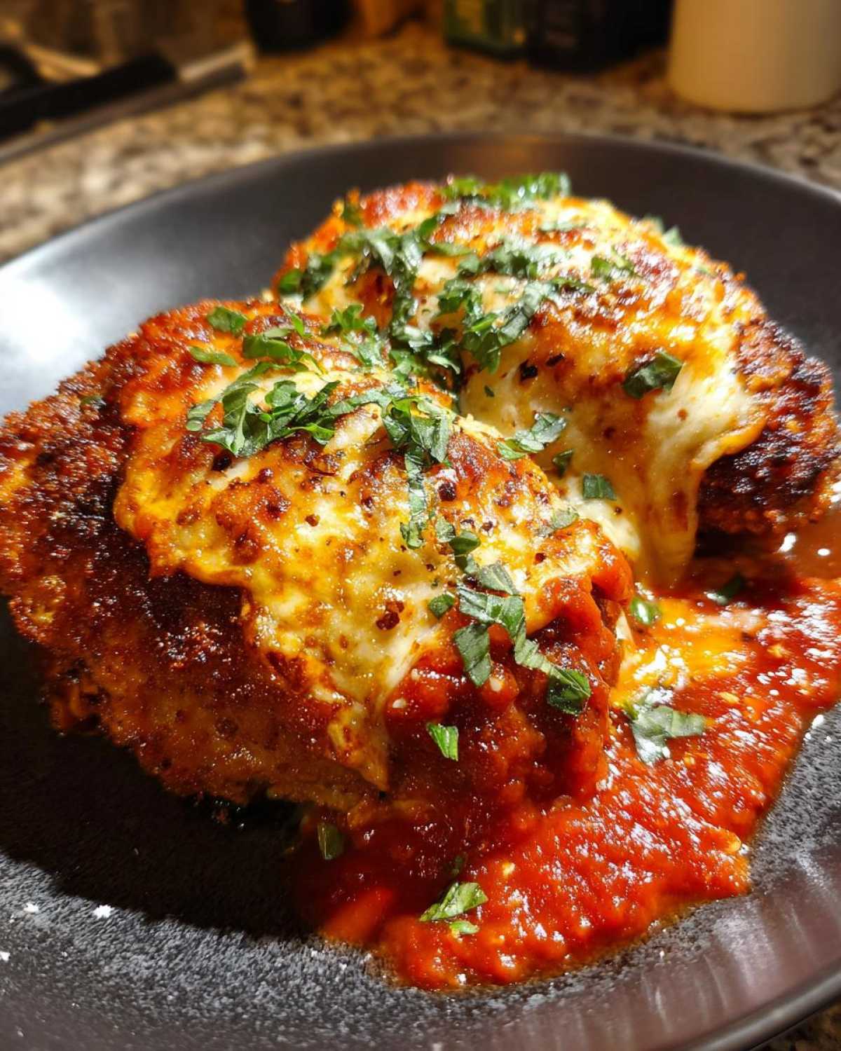 Close-up of a golden-brown breaded chicken parmesan recipe topped with melted mozzarella and fresh parsley.