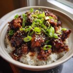 Close-up of a delicious chicken rice bowl featuring crispy, glazed chicken pieces over white rice, topped with green onions and sesame seeds.