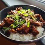Close-up of a delicious chicken rice bowl featuring glazed chicken pieces over white rice, topped with green onions and sesame seeds.