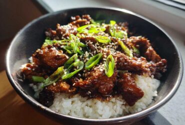 Close-up of a delicious chicken rice bowl featuring glazed chicken pieces over white rice, topped with green onions and sesame seeds.