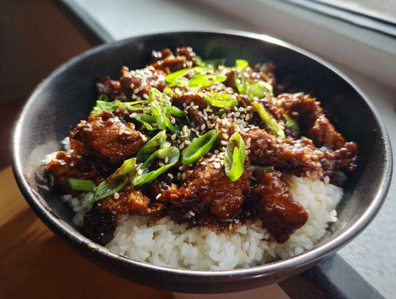 Close-up of a delicious chicken rice bowl featuring glazed chicken pieces over white rice, topped with green onions and sesame seeds.