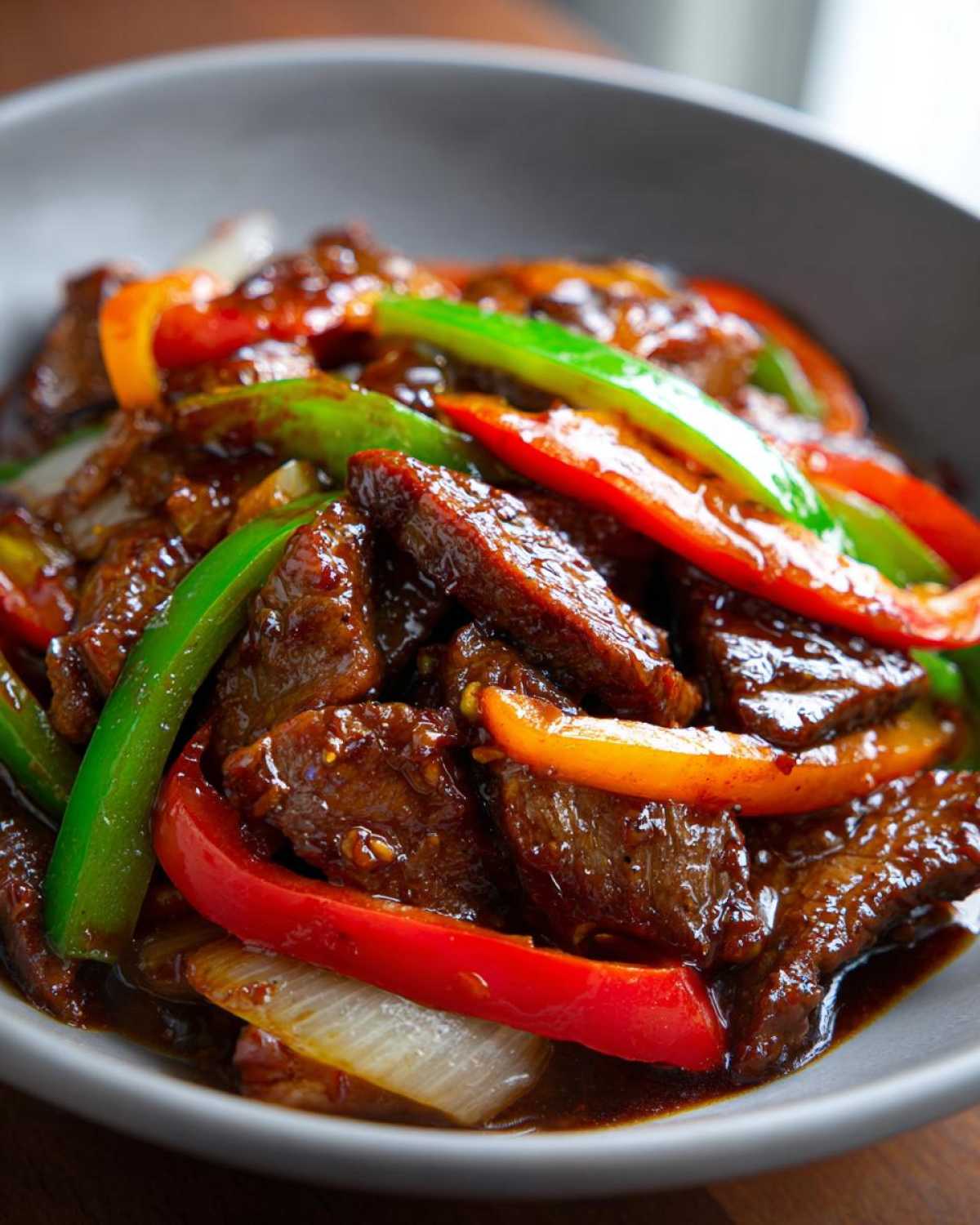 A close-up shot of savory pepper steak strips coated in dark sauce with bright red, green, and orange bell peppers.