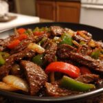 Close-up of savory pepper steak stir-fry with strips of beef, green peppers, red peppers, and onions in a dark sauce.