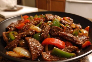 Close-up of savory pepper steak stir-fry with strips of beef, green peppers, red peppers, and onions in a dark sauce.