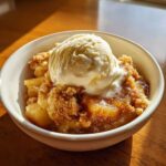 A warm serving of apple cobbler topped with a melting scoop of vanilla ice cream.