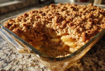 Close-up of a golden brown apple crisp recipe baked in a clear glass dish, showing the crunchy topping and soft apples.