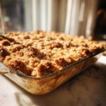 Close-up of a golden brown apple crisp recipe baked in a clear glass dish, showing the crunchy topping.