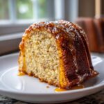 A close-up of a moist slice of bacardi rum cake drizzled with a thick, glossy caramel glaze.