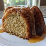 Close-up of a slice of moist bacardi rum cake topped with a thick, dripping rum glaze on a white plate.