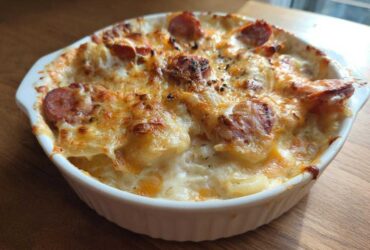 A bubbling, golden-brown baked pierogi casserole topped with melted cheese and sliced sausage.