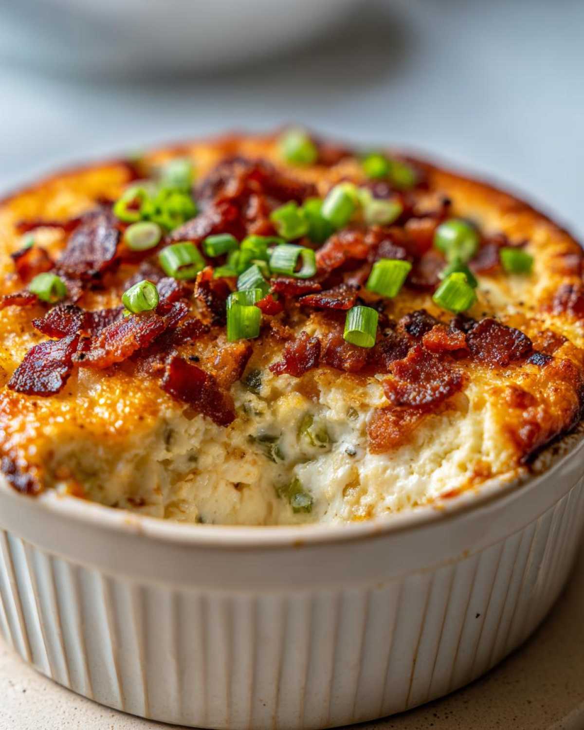 Close-up of a creamy, baked popper dip topped with crispy bacon bits and fresh green onions.