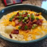 Close-up of a creamy, thick potato soup recipe topped with shredded cheddar cheese, bacon bits, and green onions.