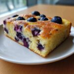 Close-up of a thick, golden slice of blueberry sheet pan pancakes topped with fresh blueberries.