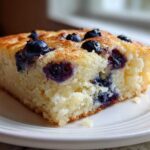 Close-up of a square slice of fluffy blueberry sheet pan pancakes served on a white plate.