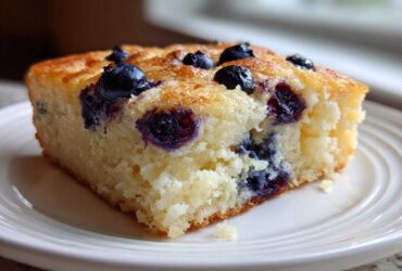 Close-up of a square slice of fluffy blueberry sheet pan pancakes served on a white plate.