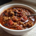 Close-up of a white bowl filled with rich, hearty high protein chili featuring ground meat and kidney beans.