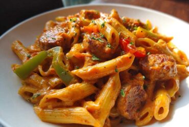 Close-up of creamy Cajun sausage pasta featuring penne, sliced sausage, green peppers, and parsley garnish.