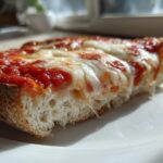 A close-up shot of a melted, cheesy english muffin pizza slice on a white plate.
