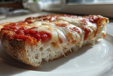 A close-up shot of a melted, cheesy english muffin pizza slice on a white plate.