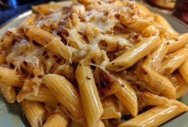 A close-up shot of penne pasta coated in a rich sauce and topped with melted, gooey cheese, characteristic of french onion pasta.