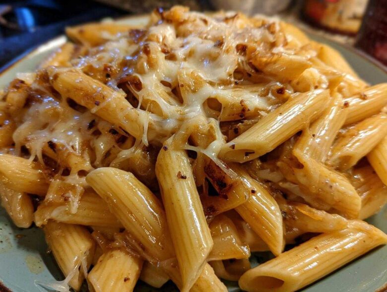 A close-up shot of penne pasta coated in a rich sauce and topped with melted, gooey cheese, characteristic of french onion pasta.