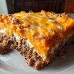 A close-up slice of cheesy meatloaf casserole topped with bright orange sweet potato mash and melted cheddar cheese.