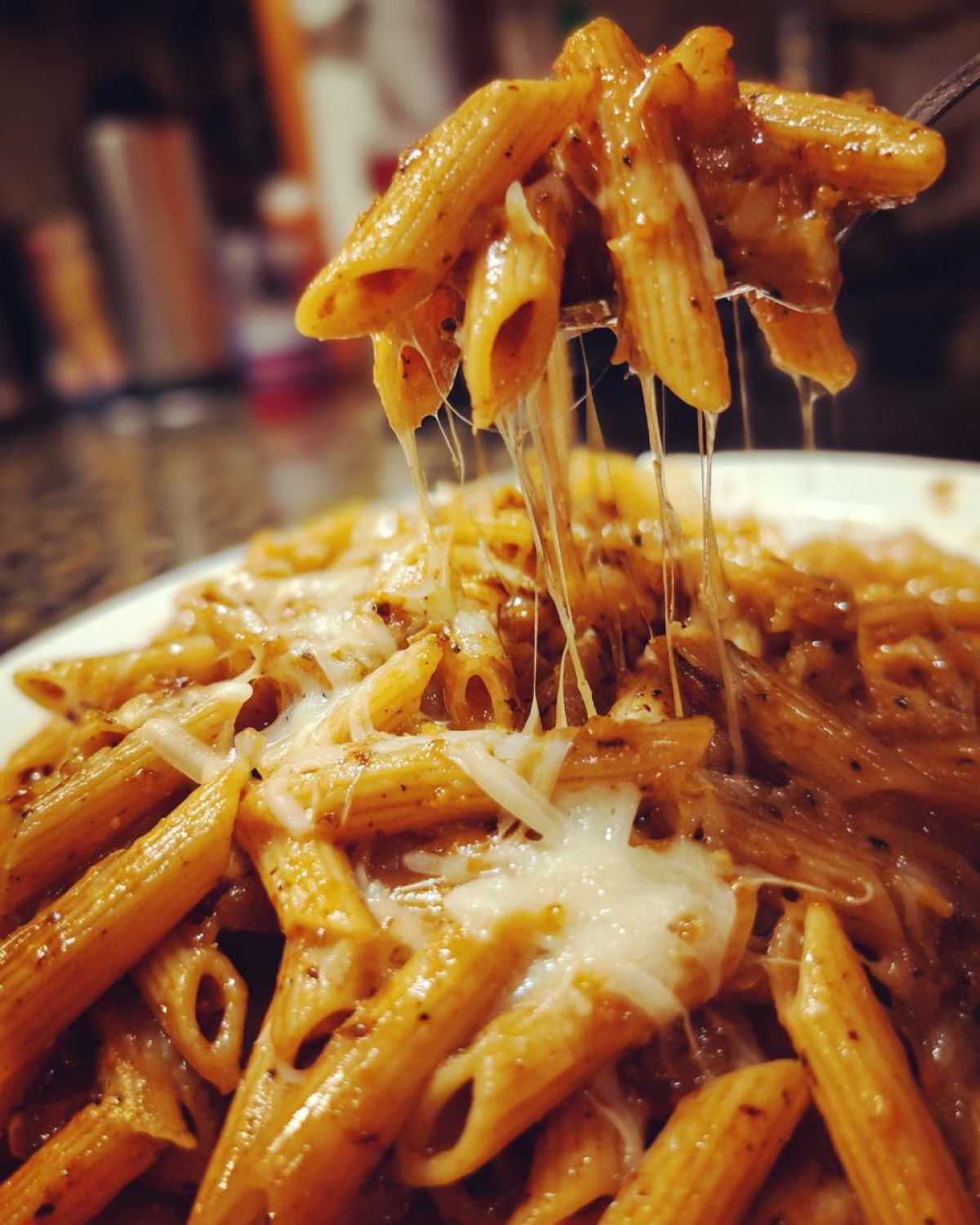 Close-up of penne pasta being lifted, showing extreme cheese pull from the rich french onion pasta sauce.