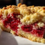 A close-up shot of a square slice of cherry dump cake showing the bright red cherry filling and crumbly topping.