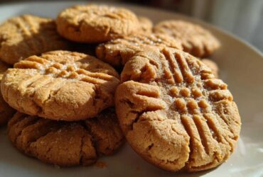 A stack of freshly baked, chewy peanut butter cookies featuring classic crosshatch fork marks and sprinkled with sugar.