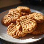 A stack of freshly baked, chewy peanut butter cookies with classic crisscross fork marks on a white plate.