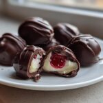 Close-up of homemade chocolate covered cherries, one cut open showing the creamy filling and cherry center.