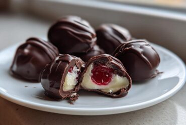 Close-up of homemade chocolate covered cherries, one cut open showing the creamy filling and cherry center.