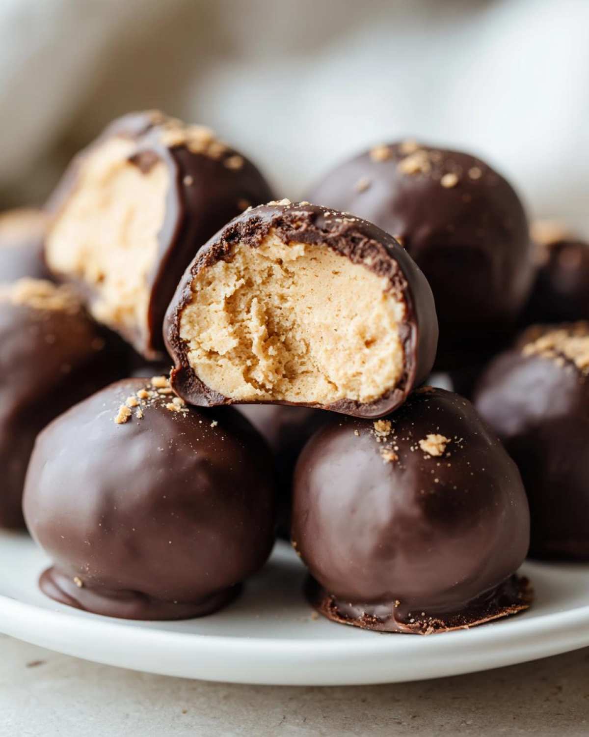 A stack of rich, chocolate-covered peanut butter balls, with one bitten in half revealing the creamy center.