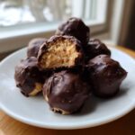 A stack of homemade peanut butter balls dipped in rich dark chocolate, one is bitten open.