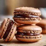 Close-up of three rich, brown chocolate macarons filled with glossy ganache.