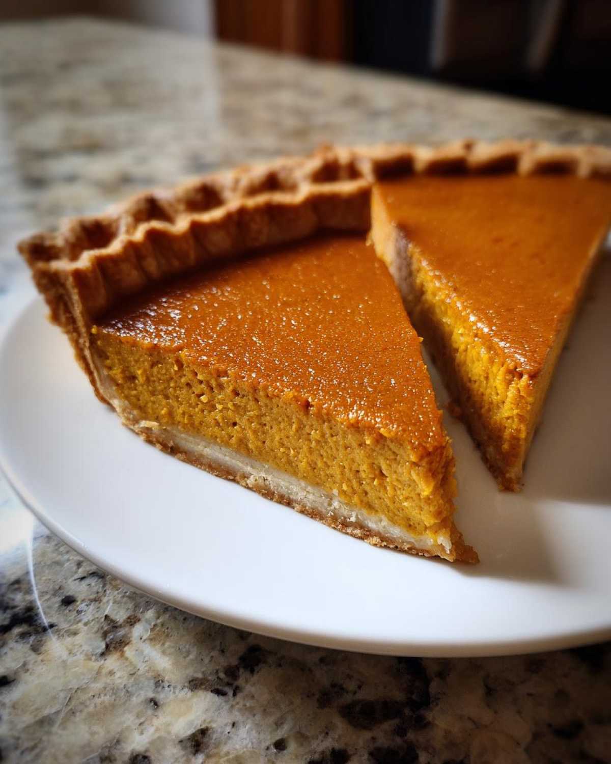 Two slices of rich orange classic pumpkin pie recipe served on a white plate.