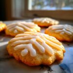 Close-up of golden baked cookies topped with a bright, glossy white cookie icing recipe, set near a window.