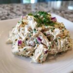 A mound of creamy cottage cheese chicken salad mixed with red onion and herbs, garnished with fresh dill.