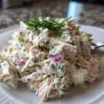 A close-up of a generous serving of cottage cheese chicken salad, mixed with celery and red onion, topped with fresh dill.