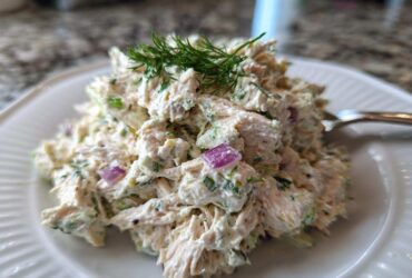 A close-up of a generous serving of cottage cheese chicken salad, mixed with celery and red onion, topped with fresh dill.