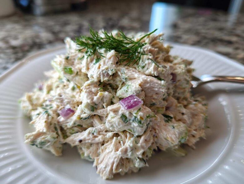 A close-up of a generous serving of cottage cheese chicken salad, mixed with celery and red onion, topped with fresh dill.